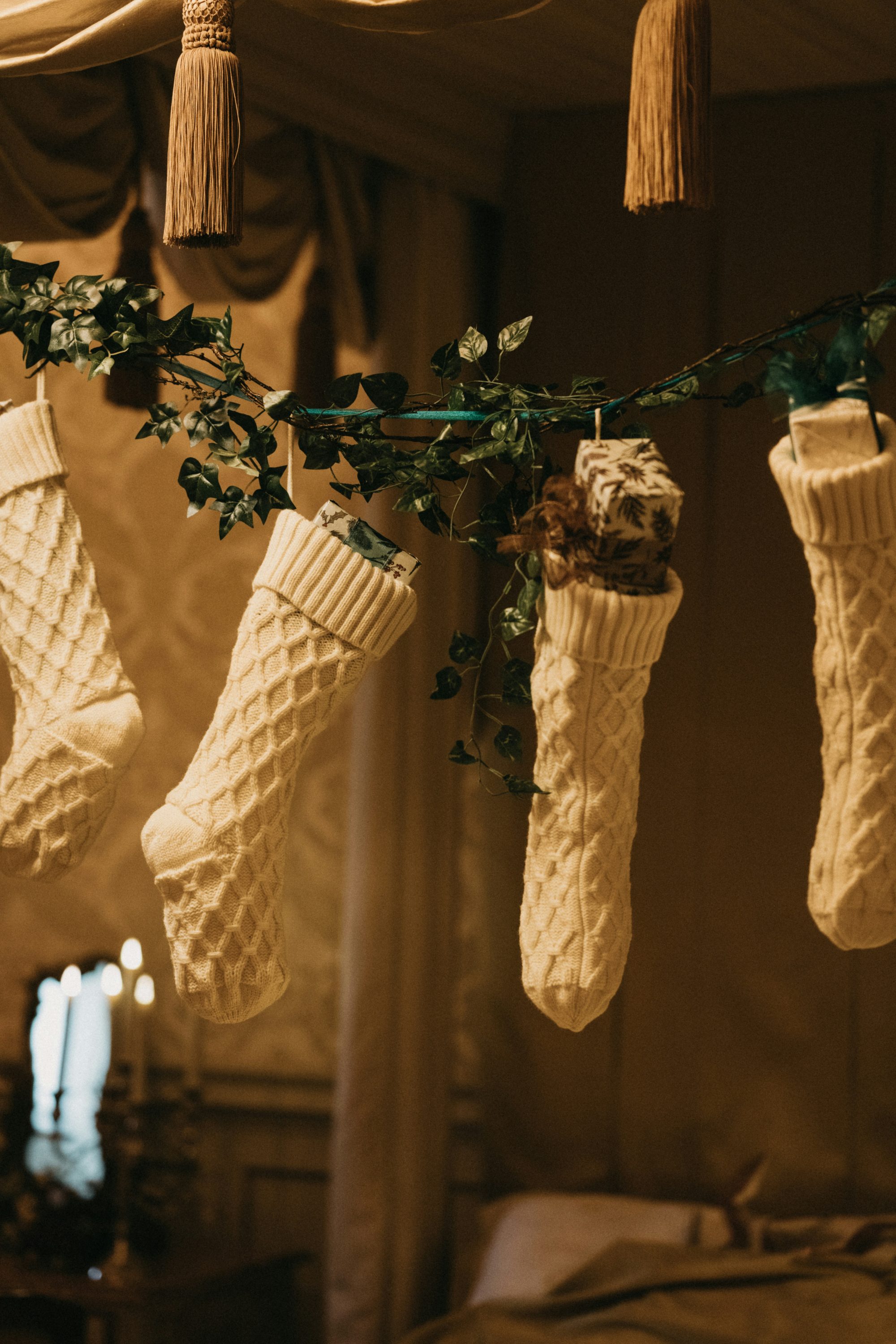 Four cream, cable-knit Christmas stockings hung on a garland, partially filled with small gifts.