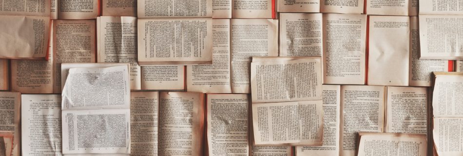An overhead, flat-lay view of numerous open books overlapping one another, covering the entire surface with aged, cream-colored pages and printed text.